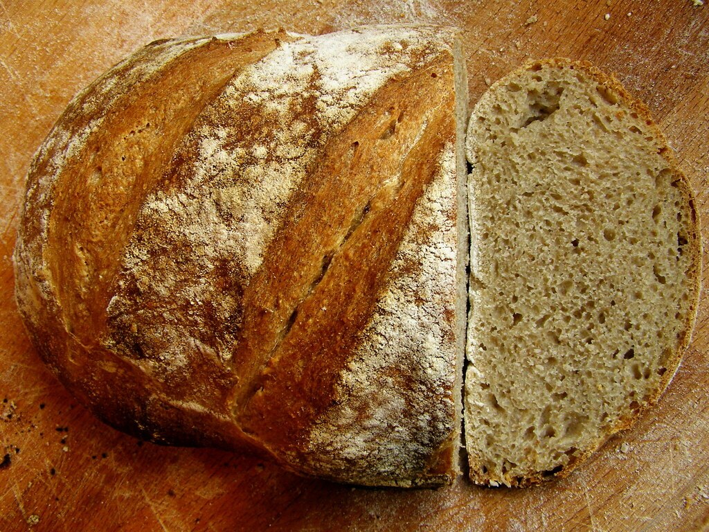 A rye loaf cut open on a wooden board, showing an open irregular crumb
