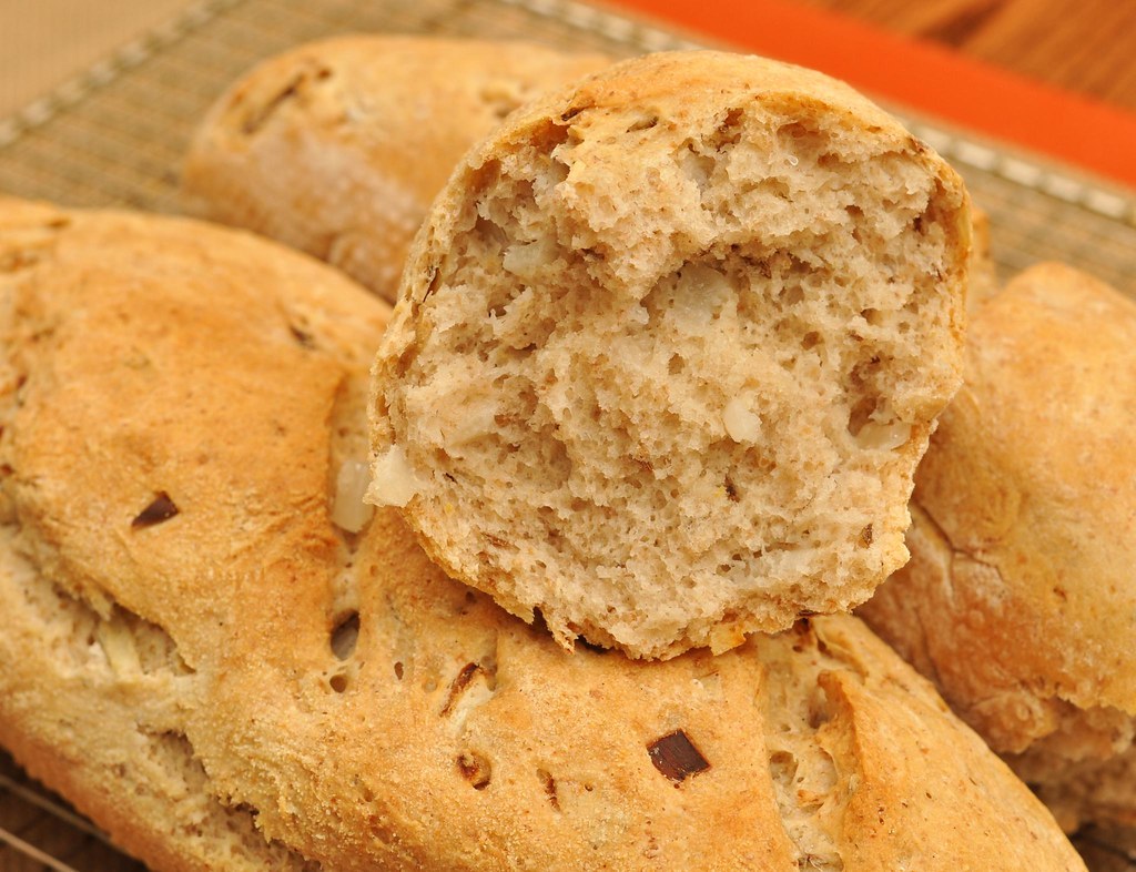 Onion rye rolls cooling on a wire rack, one broken open on top