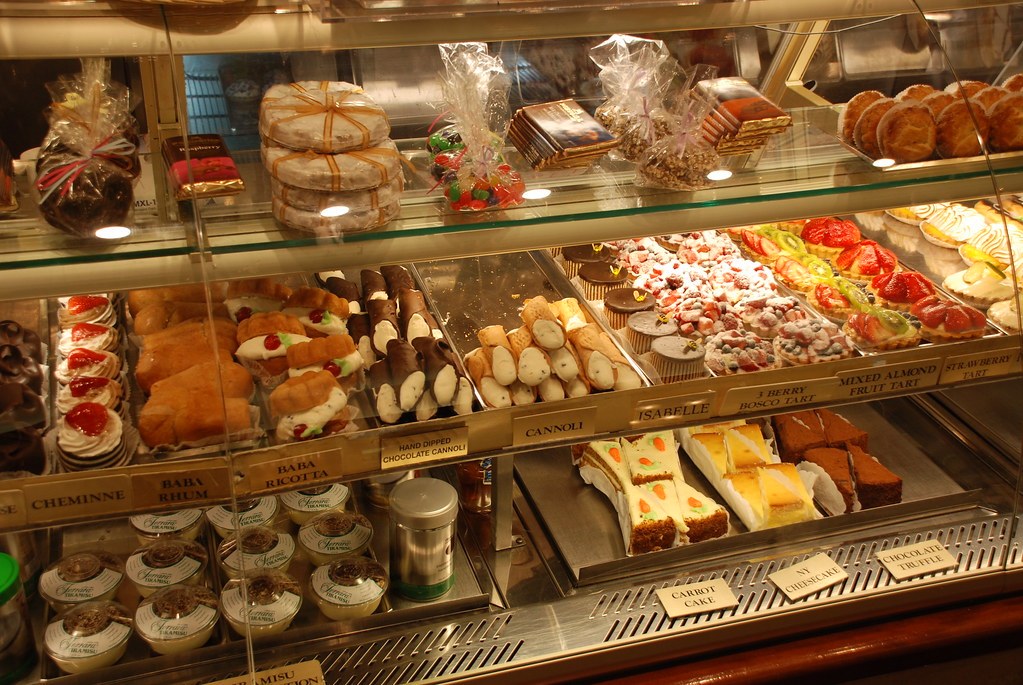 A lit glass pastry case with several tiers of cakes, tarts and pastries