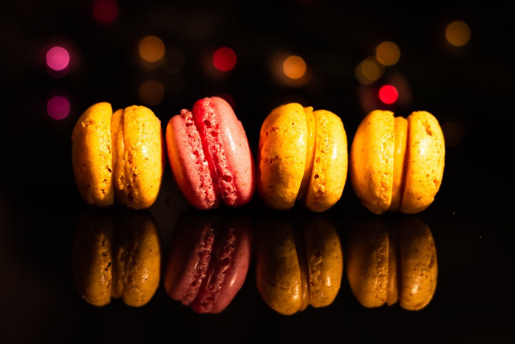 Four macarons standing in a row on a dark reflective surface